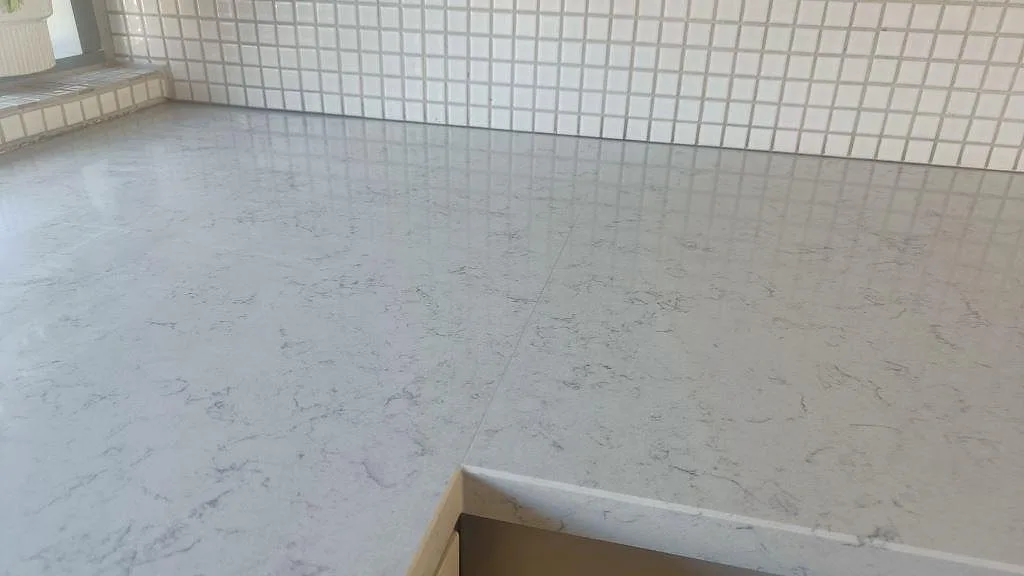 Detalj av polerad Technistone Noble Carrara med blank yta, diskret fog och vit mosaik bakom i Lund.