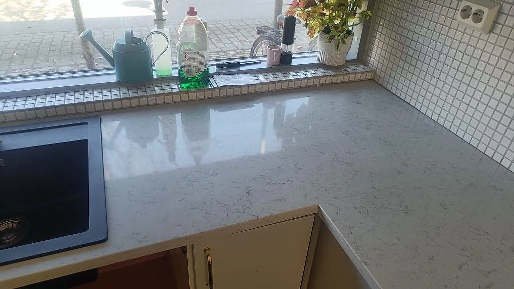 Polerad Technistone Noble Carrara som vit kompositbänkskiva med svart diskho, fönster och mosaik i ett kök i Lund.