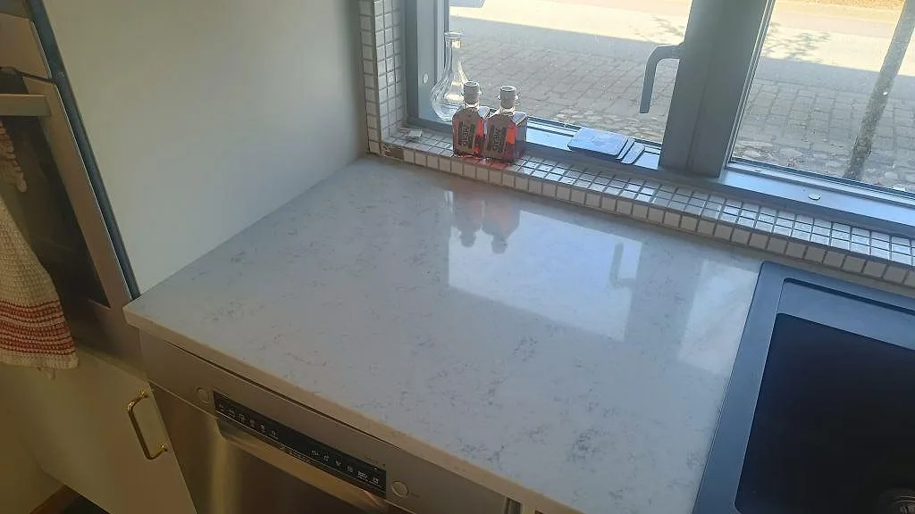 Köksbänkskiva i polerad Technistone Noble Carrara vid fönster, med svart diskho och synlig vit ådring i Lund.