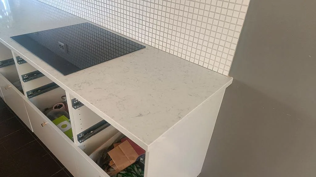Polerad kompositbänkskiva i Technistone Noble Carrara med infälld häll och vit mosaik som stänkskydd i Lund.