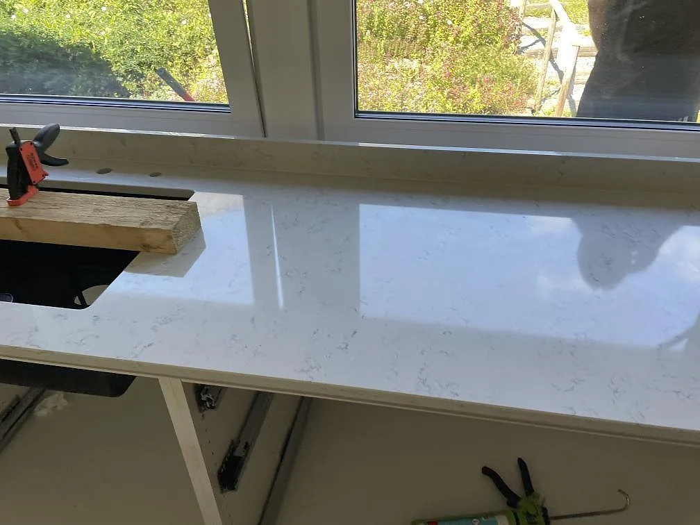 Installerad köksbänkskiva i polerad Technistone Noble Carrara med uttag för ho framför stora fönster i Lyckeby.