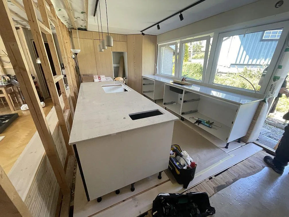 Kök under montering i Lyckeby med stor ö och lång bänkskiva vid fönster i polerad Technistone Noble Carrara.