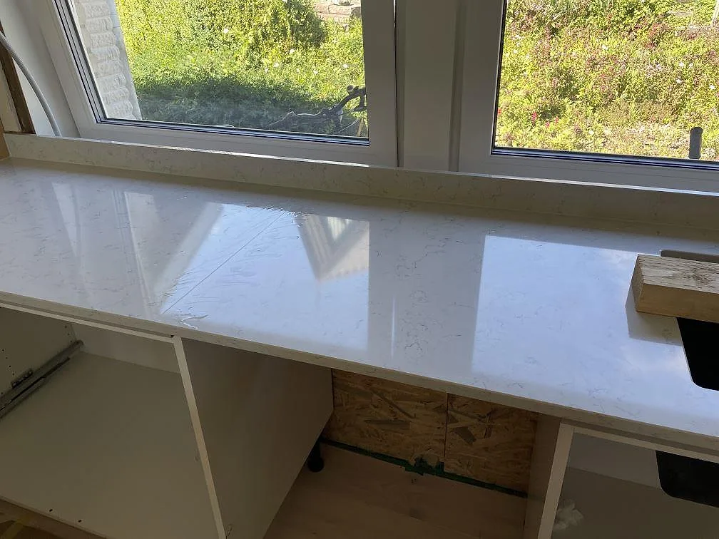 Fönstersida i kök med vit polerad Technistone Noble Carrara, låg stänkkant och synlig marmorering i Lyckeby.