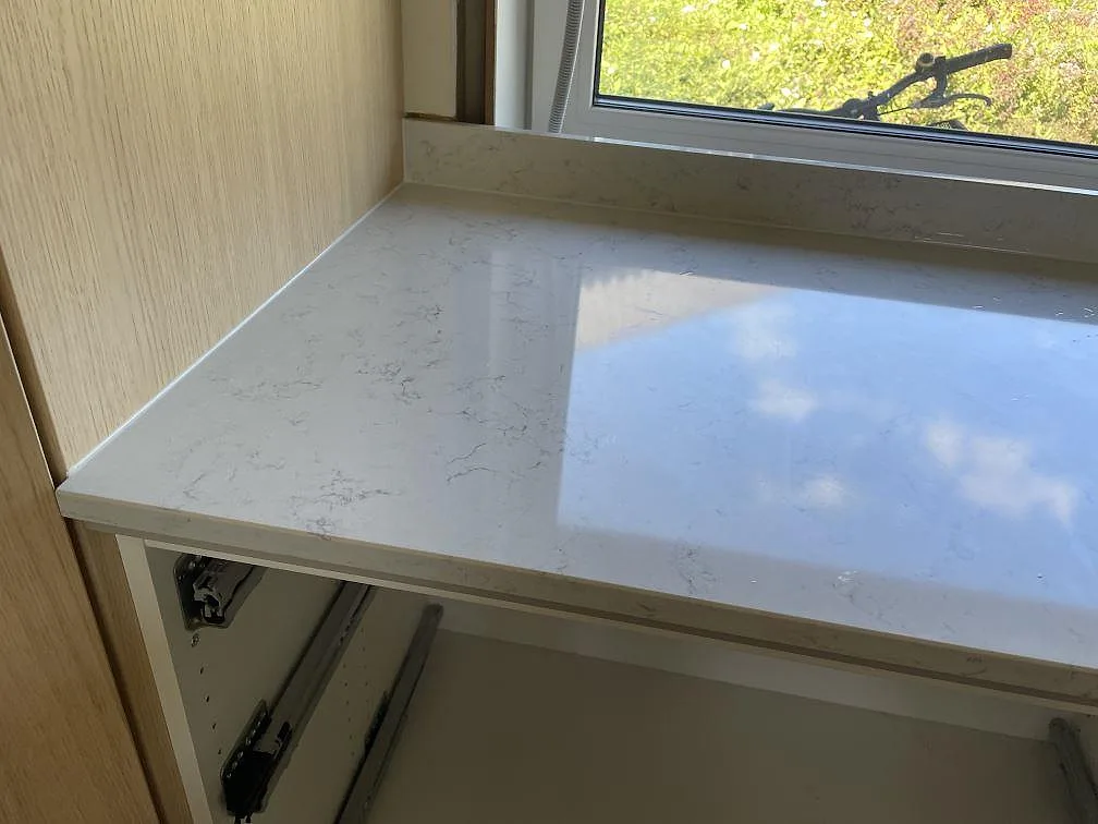 Detalj av polerad Technistone Noble Carrara vid fönster och träinredning, monterad på öppna köksstommar i Lyckeby.