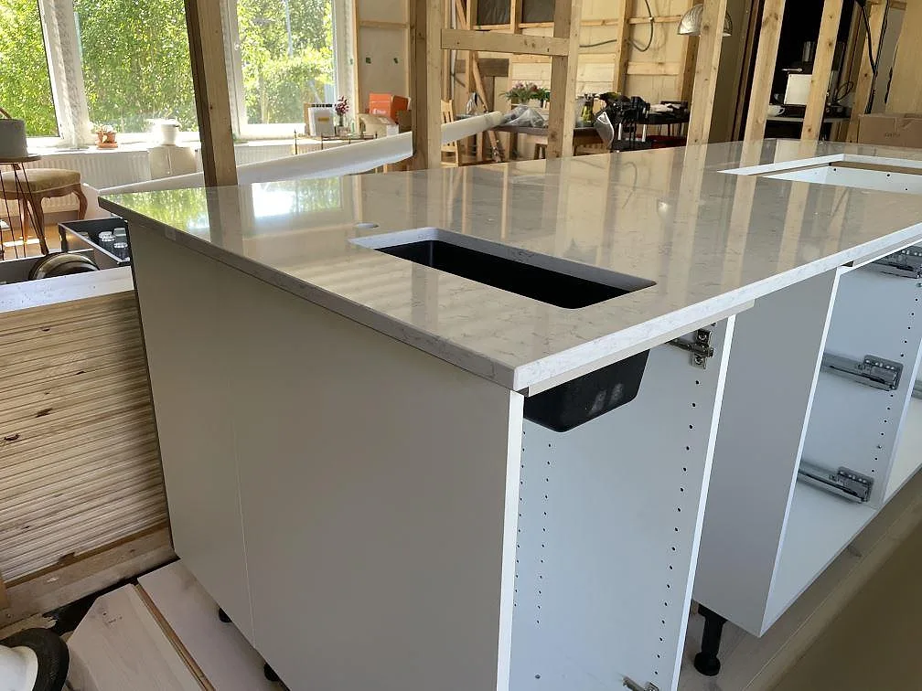 Närbild på köksö i Technistone Noble Carrara, polerad vit komposit, med hälluttag och öppna stommar i Lyckeby.