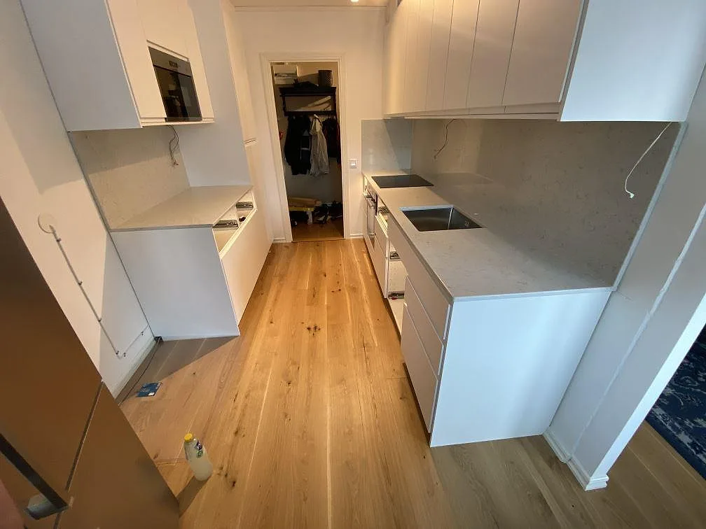 Köksbänkskiva i vit Technistone Noble Carrara, polerad, längs en vinklad köksrad med underlimmad rostfri diskho och induktionshäll i ett kök i Malmö.