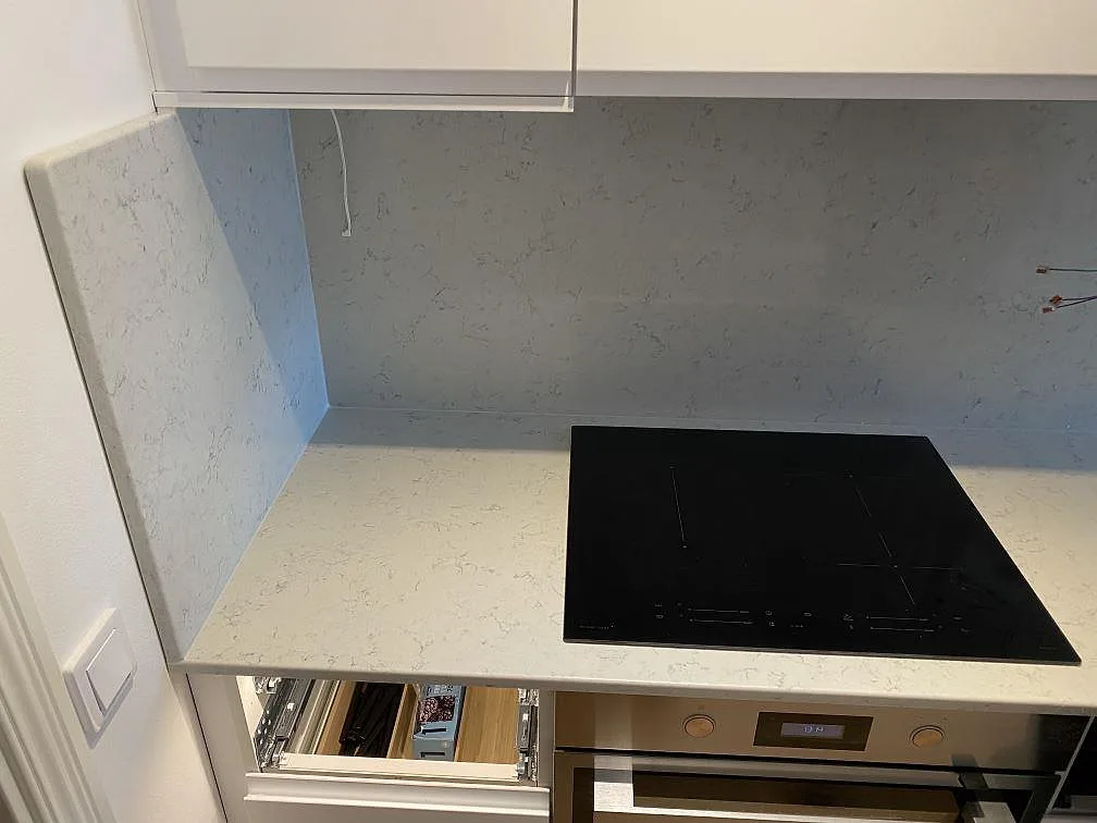 Köksbänkskiva i polerad Noble Carrara med infälld induktionshäll och stänkskydd i samma sten upp längs väggen i Malmö.