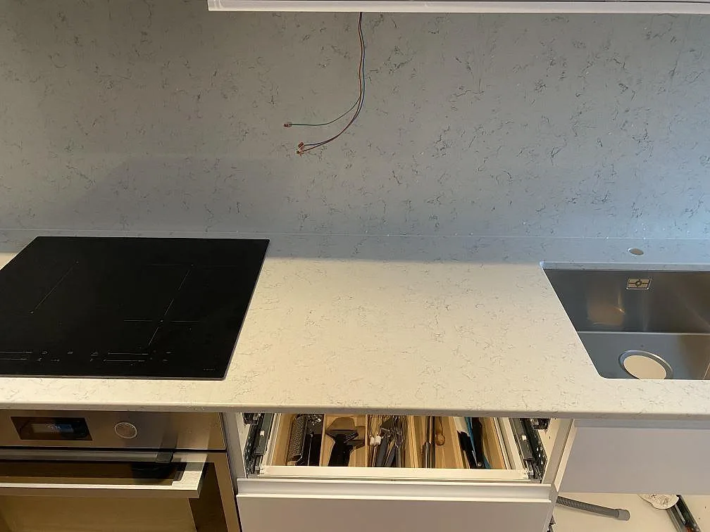 Vit Technistone Noble Carrara bänkskiva med induktionshäll och underlimmad diskho samt stänkskydd i sten i ett kök i Malmö.