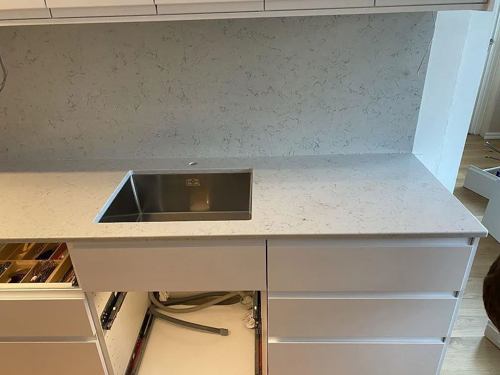 Polerad Noble Carrara köksbänkskiva med underlimmad rostfri diskho och stänkskydd i samma kvartskomposit i ett kök i Malmö.