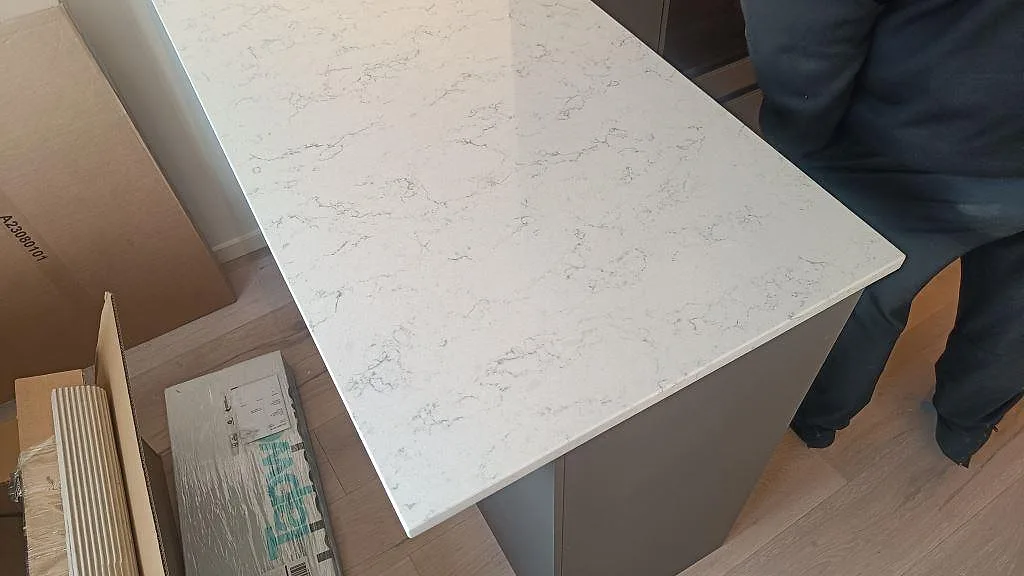Detalj av 20 mm polerad Technistone Noble Carrara på halvö med synlig ådring under montering i Malmö.