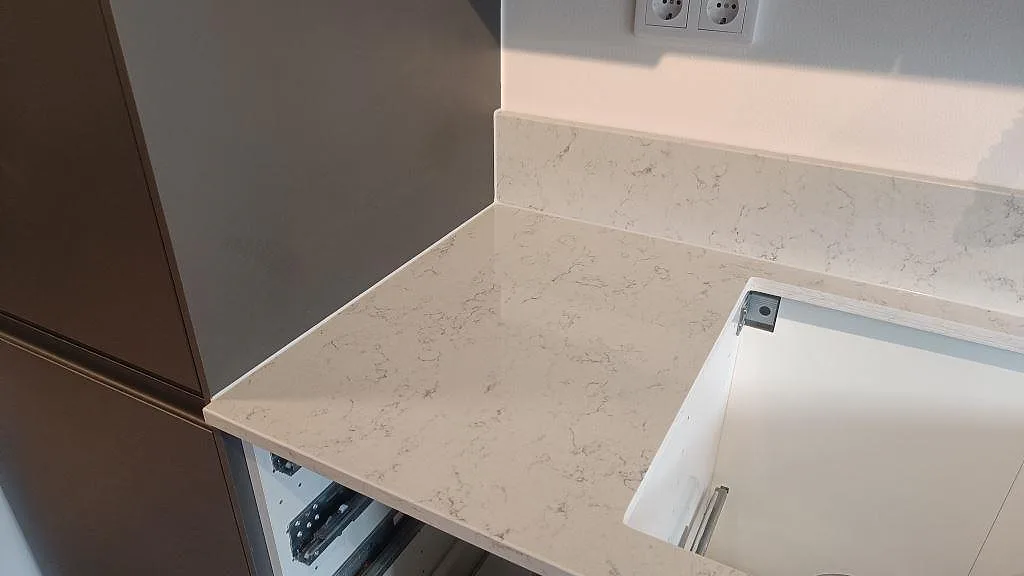 Polerad Technistone Noble Carrara som bänkskiva och stänkkant vid öppen diskbänkstomme i Malmö.