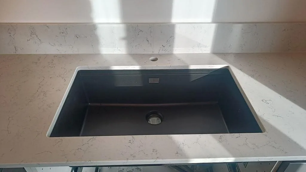 Underlimmad svart diskho i polerad Technistone Noble Carrara med uppvikt stänkkant i kök i Malmö.