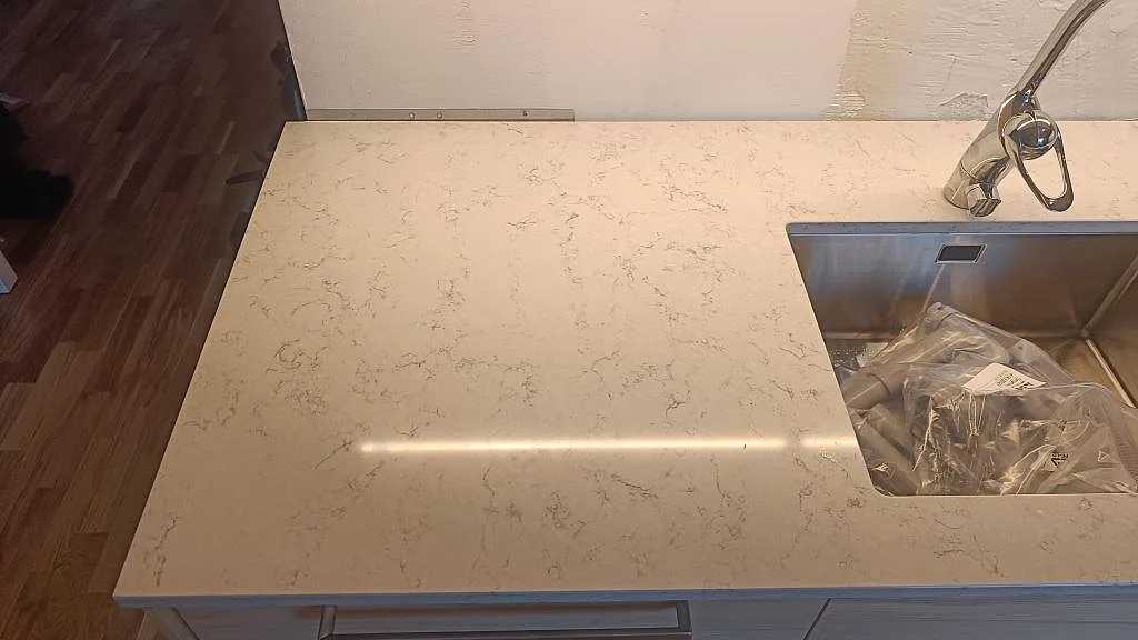 Närbild av polerad Technistone Noble Carrara som köksbänkskiva med rostfri diskho och synlig grå ådring i Malmö.