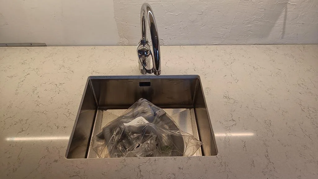 Underlimmad rostfri diskho med blandare i en polerad Technistone Noble Carrara bänkskiva under montering i Malmö.