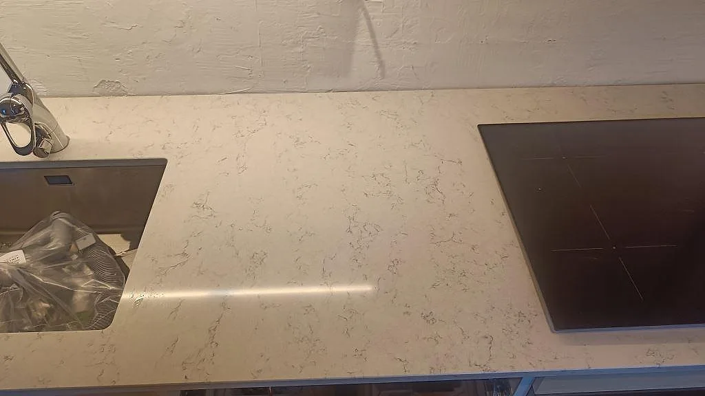 Köksbänkskiva i polerad Technistone Noble Carrara med rostfri diskho och induktionshäll på samma bänkrad i Malmö.