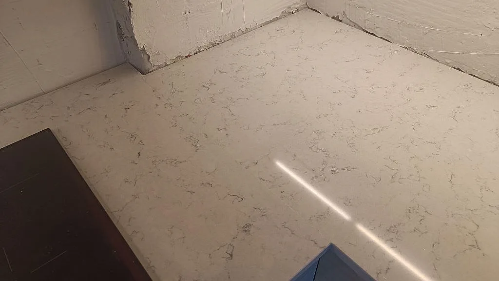 Hörndetalj av polerad Technistone Noble Carrara i ett kök, med varmvit komposit och fin grå ådring i Malmö.
