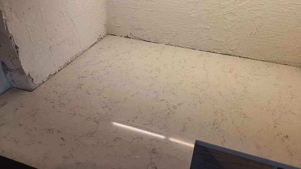 Installerad hörnyta i Technistone Noble Carrara, polerad kompositbänkskiva mot ofärdig vägg under montering i Malmö.
