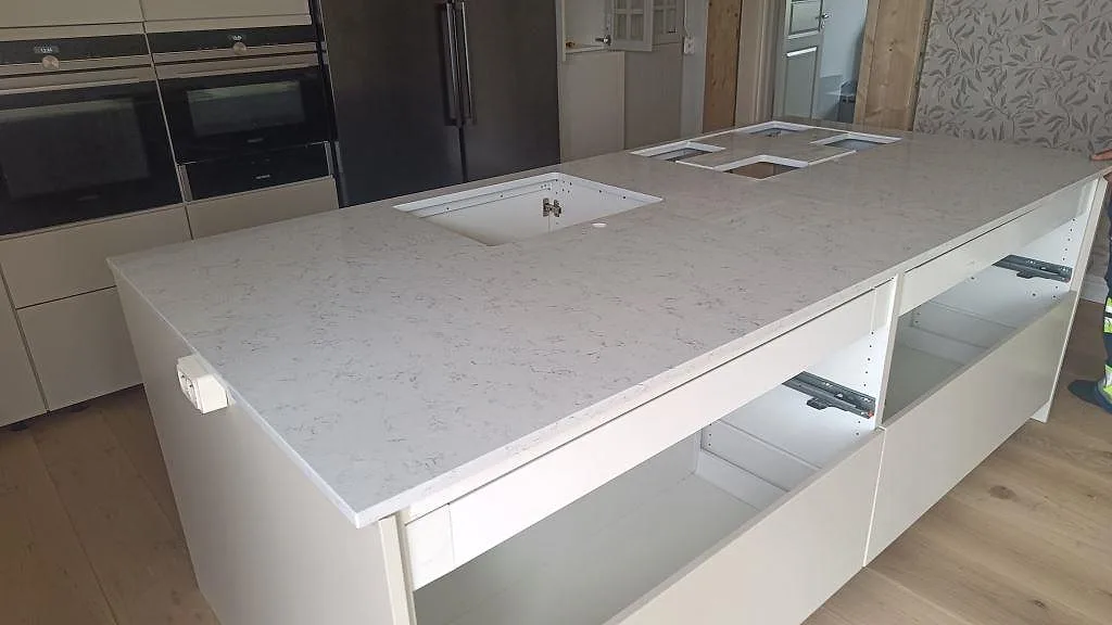 Köksbänkskiva i vit Technistone Noble Carrara, polerad kvartskomposit, monterad på en stor köksö i Mörrum.