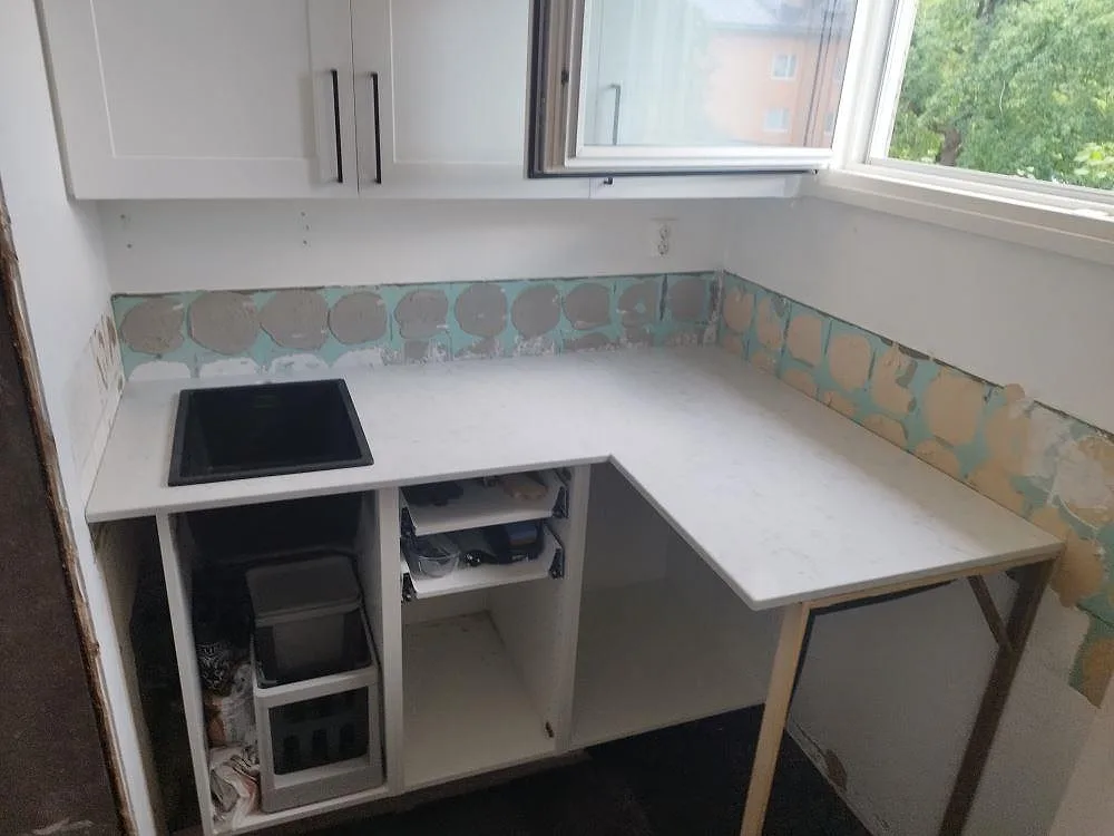 Köksbänkskiva i vit Technistone Noble Carrara kvartskomposit, polerad, med induktionshäll och mintgrön mosaik i ett kök i Nacka.