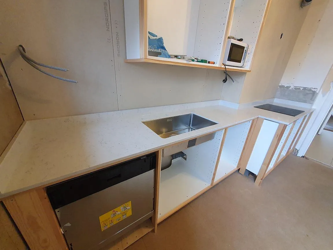 Lång köksbänkskiva i Technistone Noble Carrara, polerad, med rostfri diskho och ljus marmorering under montering i Örebro.