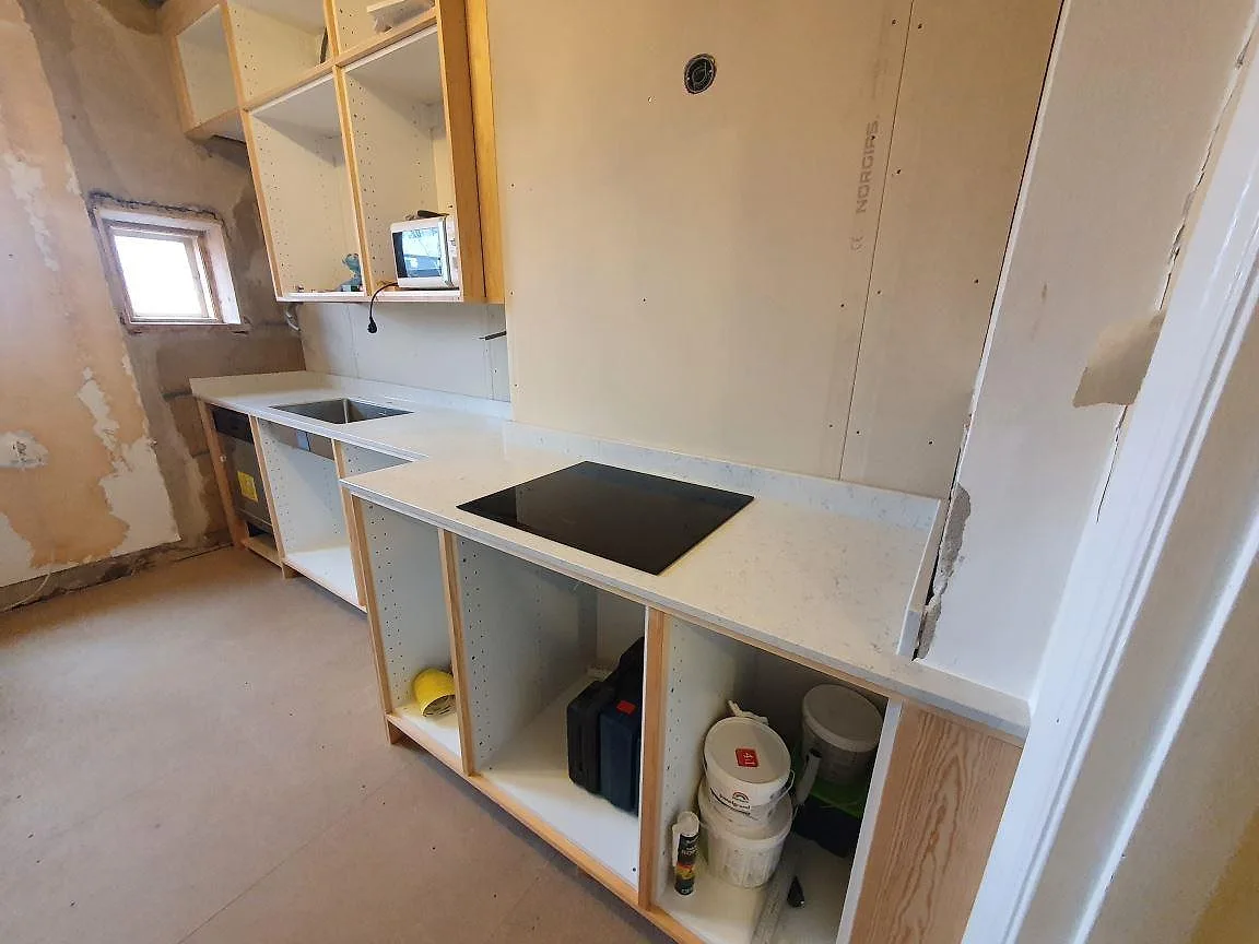 Polerad köksbänkskiva i vit Technistone Noble Carrara med underlimmad rostfri diskho och svart induktionshäll, fotad under montering i Örebro.