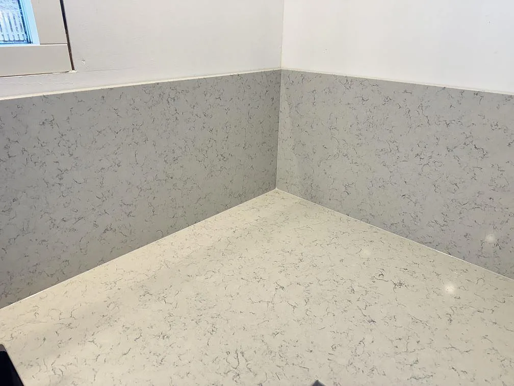 Hörn med bänkskiva och uppvikt stänkskydd i polerad Technistone Noble Carrara komposit i Partille.