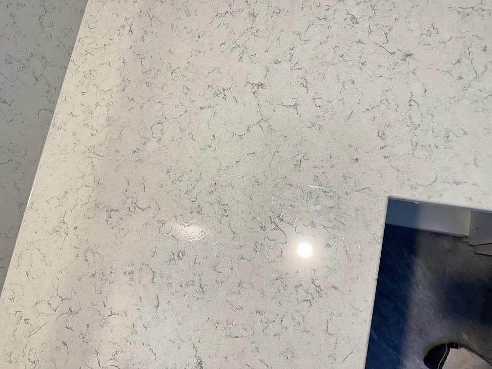 Topvy av ljus polerad Technistone Noble Carrara komposit med grå ådring och rektangulärt urtag i Partille.