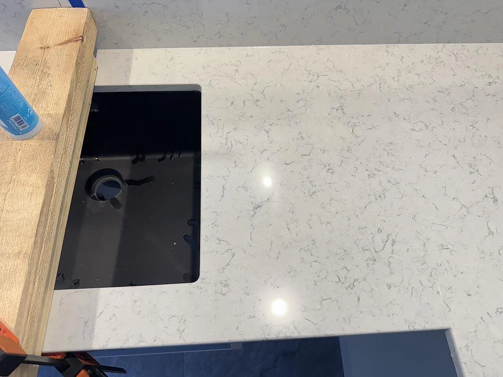 Polerad Technistone Noble Carrara köksbänkskiva med mörk diskhozon och synlig komposityta under montering i Partille.