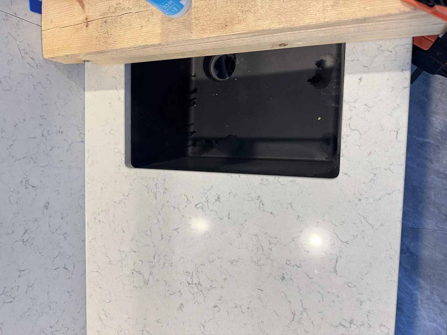 Detalj av Technistone Noble Carrara bänkskiva kring diskhozon, polerad komposit med grå ådring i Partille.