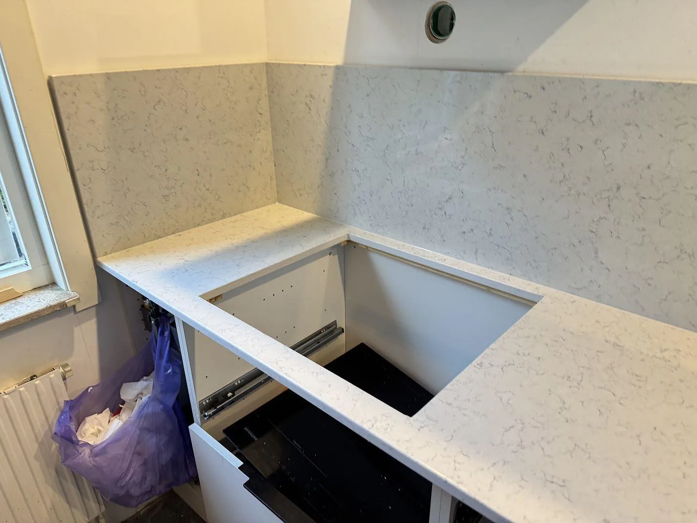 Polerad köksbänkskiva i Technistone Noble Carrara komposit med urtag och uppvikt stänkskydd under montering i Partille.