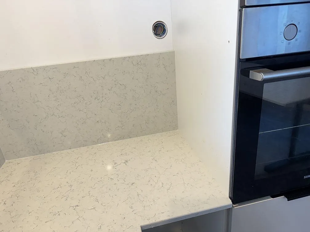 Närbild av polerad Technistone Noble Carrara bänkskiva och stänkskydd bredvid ugn i ett kök i Partille.