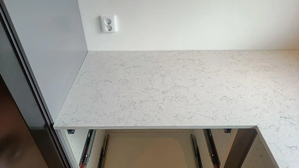 Polerad köksbänkskiva i Technistone Noble Carrara med diskret grå ådring och hörnskarv vid vägguttag i ett kök i Staffanstorp.
