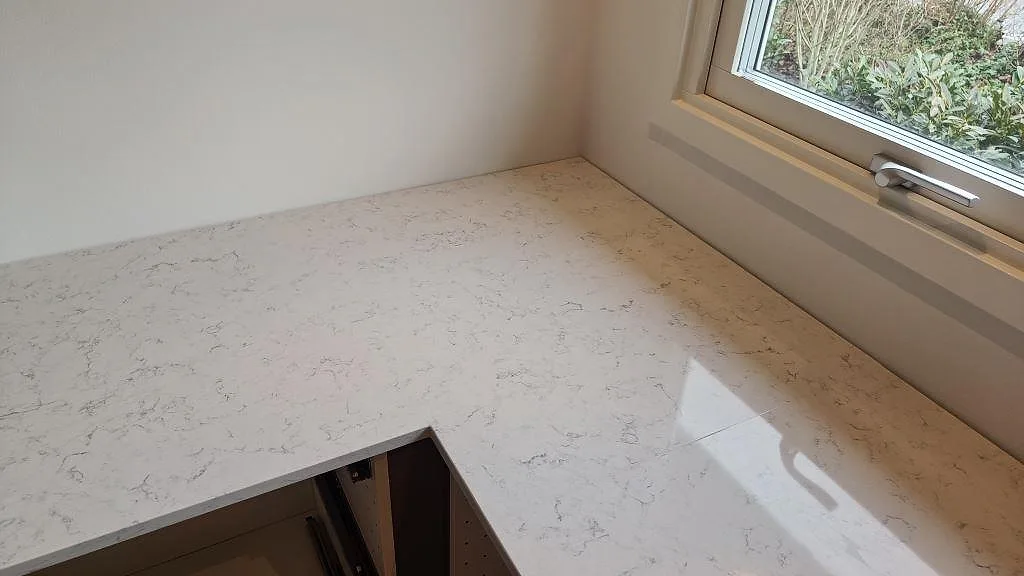 Ljus köksbänkskiva i Technistone Noble Carrara vid fönsterbänk, polerad yta med fin ådring i ett kök i Staffanstorp.