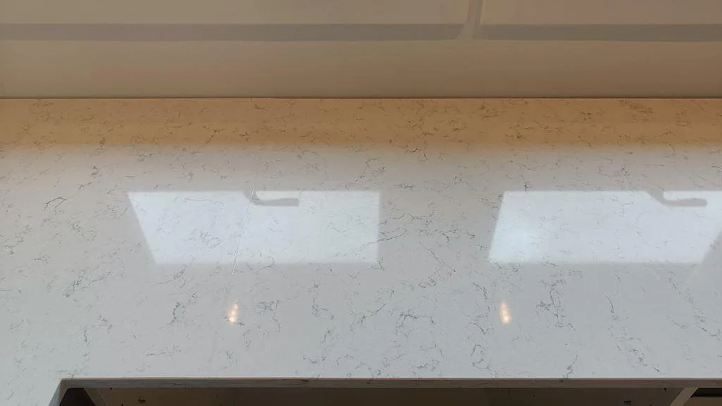 Polerad köksbänkskiva i Technistone Noble Carrara med spegelblanka fönsterreflexer och grå ådring i ett kök i Staffanstorp.