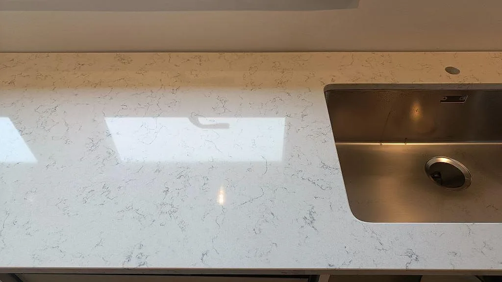 Närbild på den polerade ytan i Technistone Noble Carrara med ljusreflexer från fönstren i ett kök i Staffanstorp.