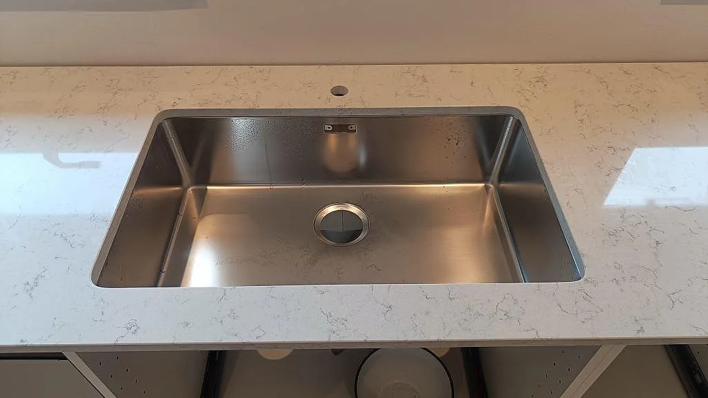 Underlimmad rostfri diskho infälld i köksbänkskiva av Technistone Noble Carrara, polerad, i ett kök i Staffanstorp.