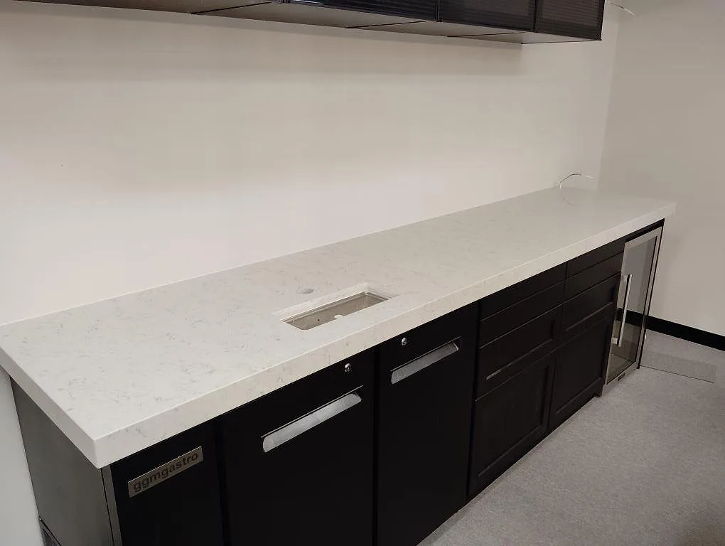 Köksbänkskiva i vit Technistone Noble Carrara, polerad kvartskomposit, monterad på mörka stommar i ett kök i Stockholm.