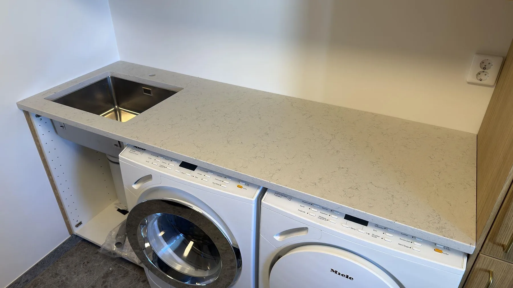 Bänkskiva i vit Technistone Noble Carrara, polerad kvartskomposit med grå ådring, med underlimmad rostfri diskho i en tvättstuga i Trångsund.