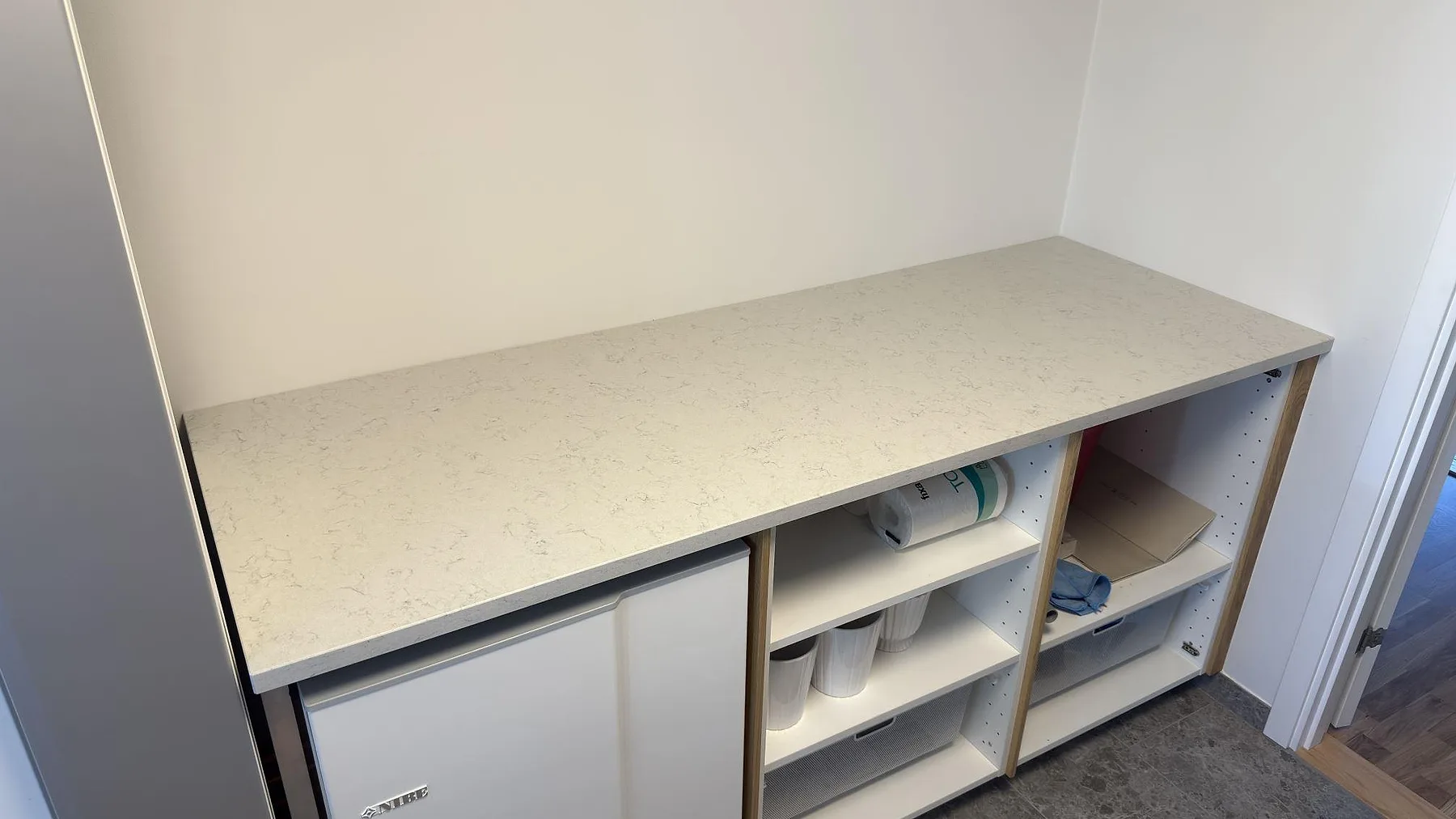 Måttanpassad bänkskiva i Technistone Noble Carrara, polerad, i en sammanhållen längd över förvaring och vitvaror i ett grovkök i Trångsund.