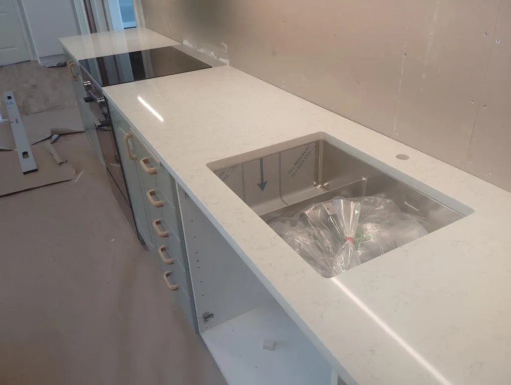 Polerad köksbänkskiva i Technistone Noble Carrara med underlimmad diskho och häll under montering i Tullinge.
