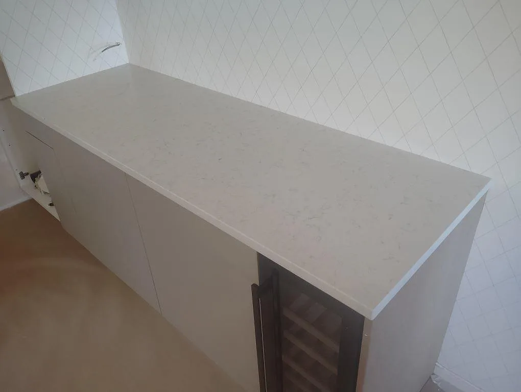 Sidobänk i vit Technistone Noble Carrara, polerad kompositsten, med rak kant och ljus köksvägg i Tullinge.