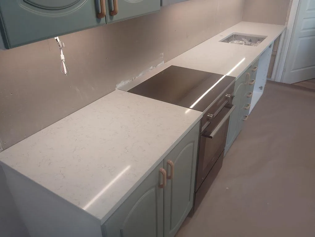 Köksbänkskiva i vit Technistone Noble Carrara, polerad kompositsten, med häll och diskho i ett kök i Tullinge.