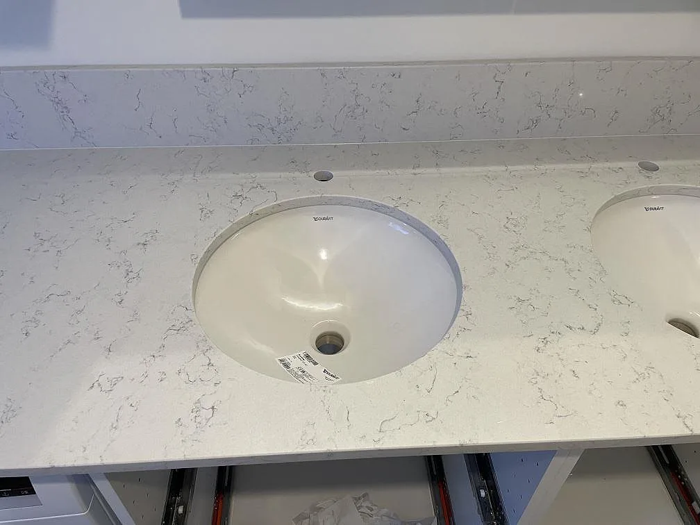 Närbild på polerad Technistone Noble Carrara med underlimmat vitt tvättställ, blandarhål och uppvikt stänkkant i badrum i Uppsala.