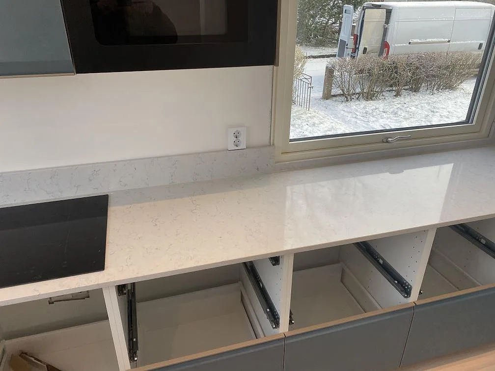 Rak bänkskiva i polerad Technistone Noble Carrara med infälld häll, uppvikt stänkkant och öppna underskåp i Värnamo.