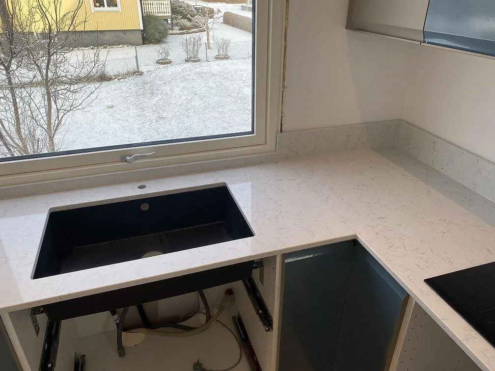 Polerad kompositskiva i Technistone Noble Carrara med svart diskho ovanpå stenen och uppvikt stänkkant vid fönster i Värnamo.
