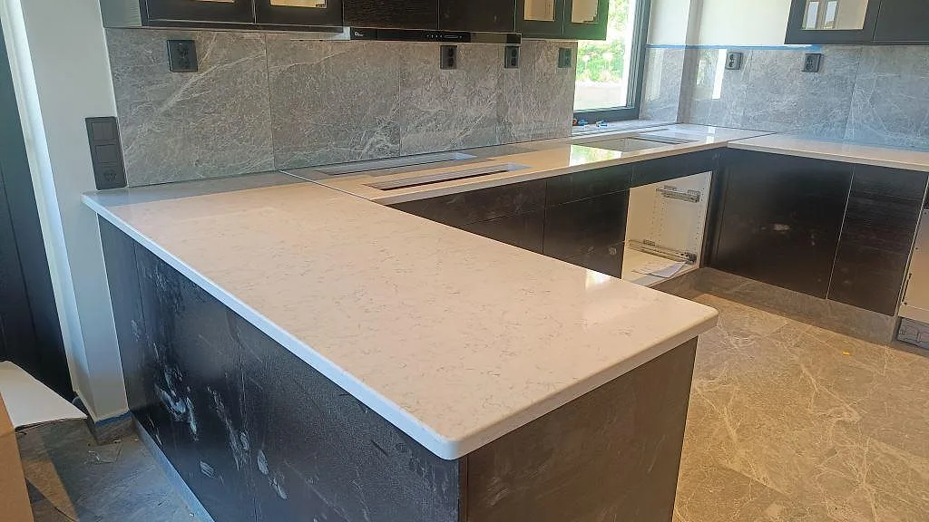 U-format kök i Växjö med polerad 30 mm Technistone Noble Carrara som ljus köksbänkskiva på mörka skåp.