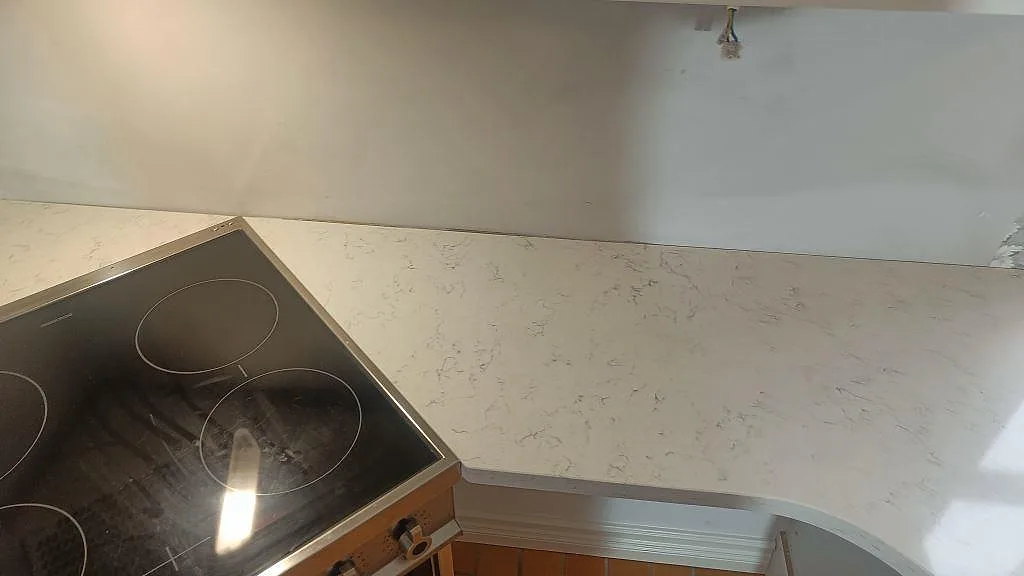 Köksbänkskiva i polerad Technistone Noble Carrara med spis intill och ljus vägg under montering i Växjö.