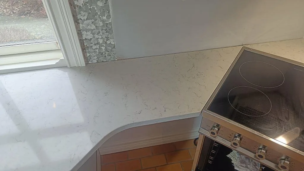 Polerad bänkskiva i Technistone Noble Carrara med rundad kant vid fristående spis och fönster i Växjö.