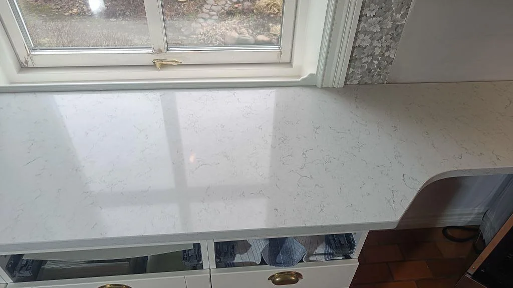 Köksbänkskiva i polerad Technistone Noble Carrara, vit kvartskomposit, under fönster i ett kök i Växjö.