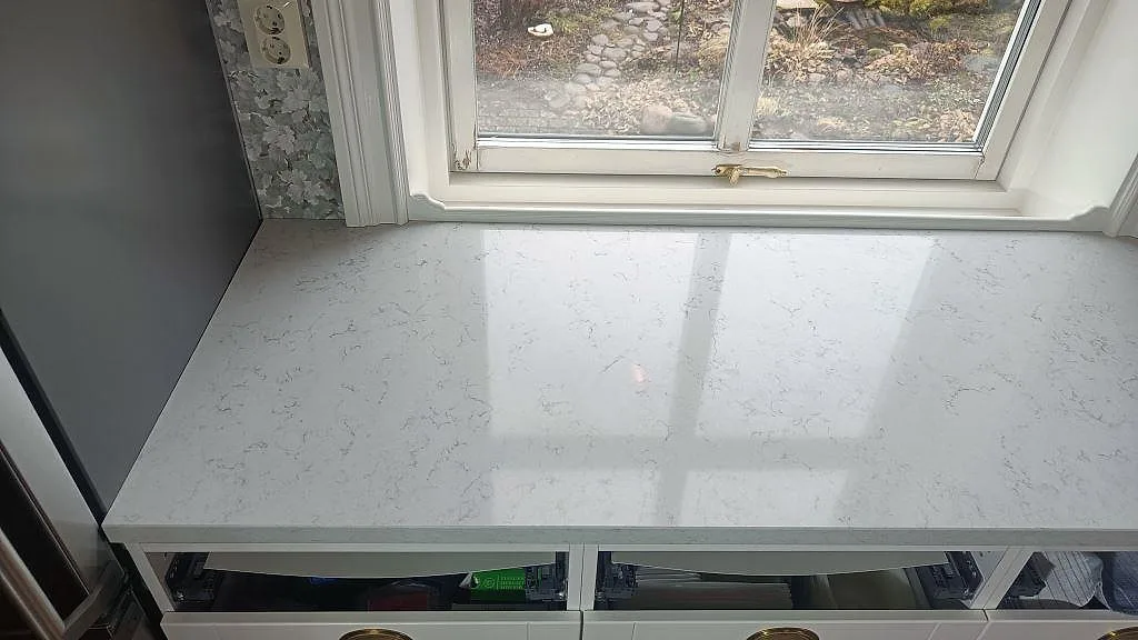 Polerad vit kvartskomposit i Technistone Noble Carrara som bänkskiva framför fönster i kök i Växjö.